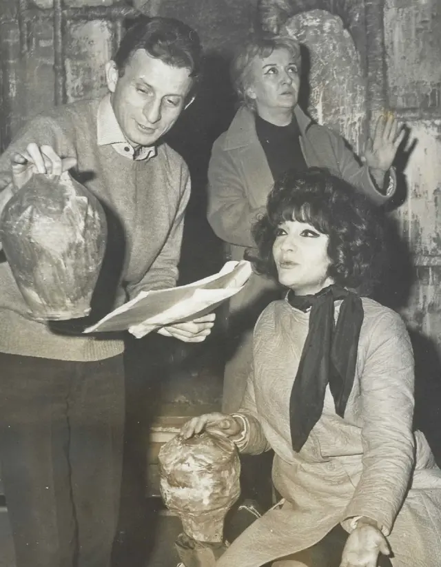 Siyah beyaz fotoğraf. Bir erkek ve iki kadın oyuncu notlarına bakıyor, biz vazoyu inceliyor