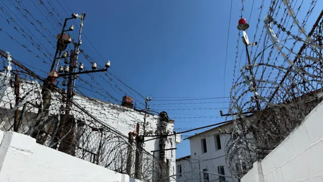 Paredes brancas cobertas de arame farpado, em dia de céu azul