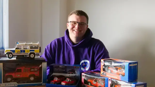 Gülümseyen bir adam, Land Rover modellerinden oluşan koleksiyonunun arkasında oturuyordu.