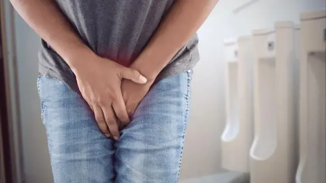 Un homme dans un urinoir se tord de douleur