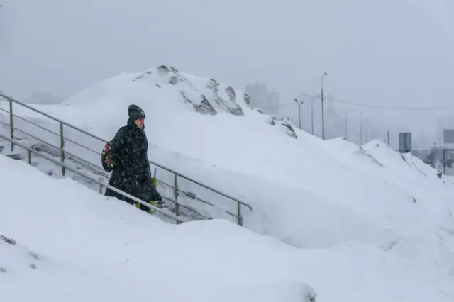 женщина спускается по лестнице рядом с гигантским сугробом снега