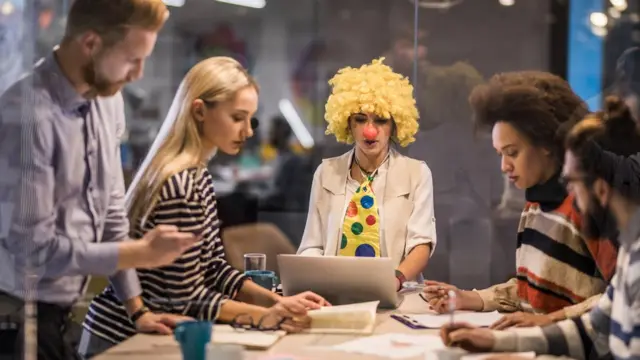 Una mujer con peluca y corbata de payaso en reunión de trabajo