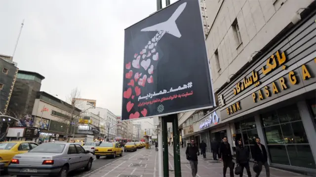Les gens passent devant une bannière sur un lampadaire à Téhéran disant : "nous sommes tous dans la douleur et la sympathie."