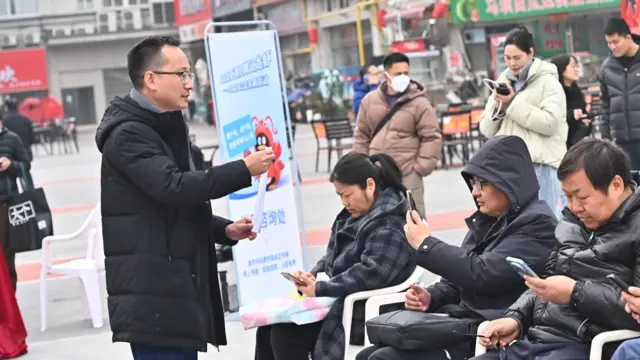 左边一男士举着一张纸，面对着右边两位男士一位女士，他们低头看手机。