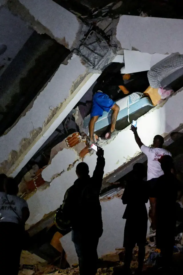 Hombre busca sobreviviente en los escombros y otros alumbran con sus celulares en La Guaira, Venezuela.