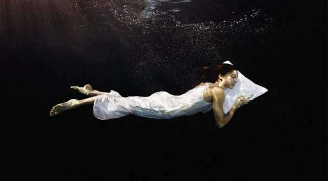 Une femme est allongée dans une eau noire. Elle a la tête posée sur un oreiller