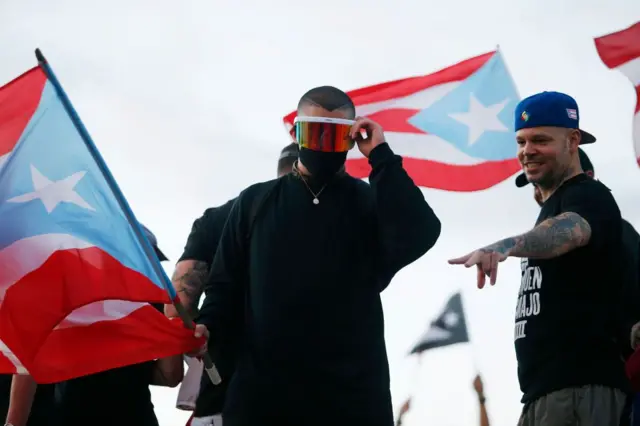 المغنيان "ريزيدينتيه" (على اليمين) و"باد باني" (على اليسار) ينضمان إلى آلاف المتظاهرين المحتجين ضد ريكاردو روسيلو، حاكم بورتوريكو في 17 يوليو/تموز 2019 أمام مبنى الكابيتول في سان خوان القديمة، بورتوريكو.