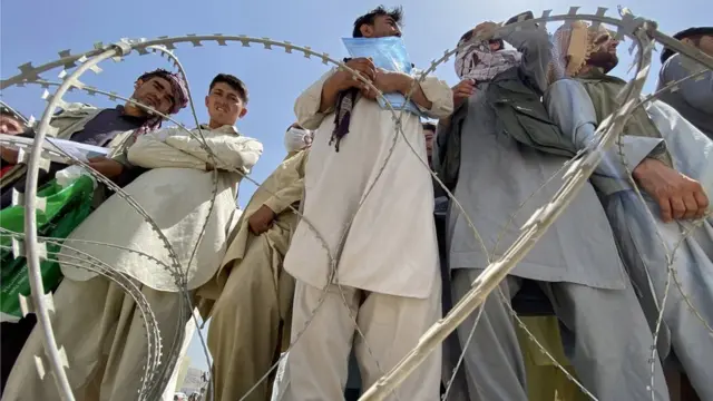 أفغان يقفون وراء أسلاك شائكة في المطار.