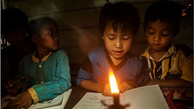 Tiga orang anak belajar dengan penerangan lilin.