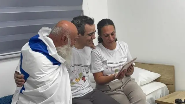 ኦምሪ ኣብ ማእከል፡ ብሓደ ወገን ባንዴራ እስራኤል ኣብ ዝባኑ ዝገበረ ኣቦኡ፡ በቲ ሓደ ወገን ድማ ሰበይቱ ኣብ ኣይፓድ እናተመልከቱ