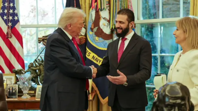 President Tramp Ahmad Ash-Sharaa bilan qo'l silkiyapti.