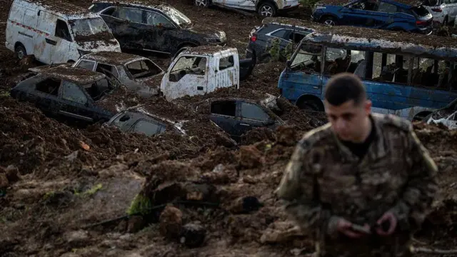 جندي لبناني خلفه سيارات متضررة ومغطاة بالتراب متوقفة في مرآب