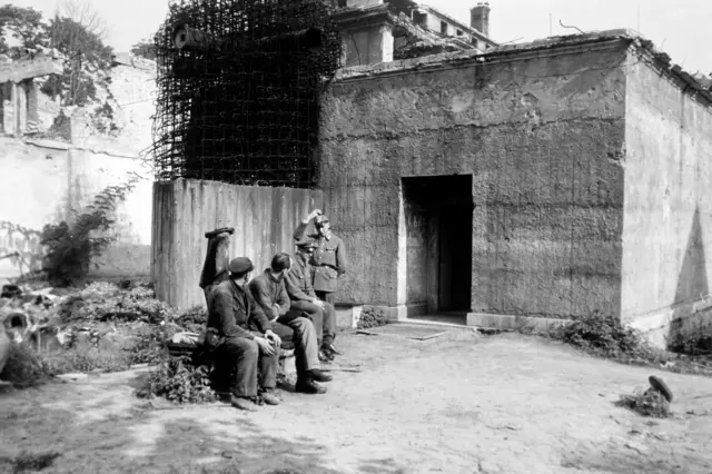 În fotografia alb-negru se văd soldați care păzesc, în 1946, Führerbunkerul, unde Adolf Hitler și Eva Braun s-au sinucis.