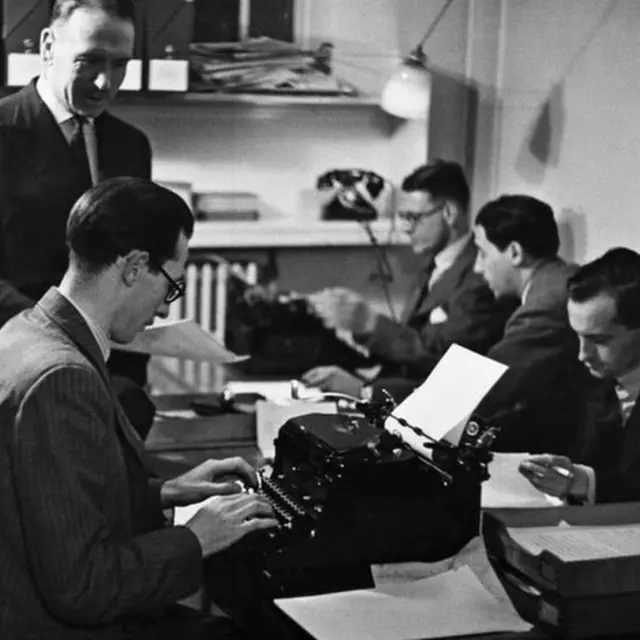 Hombres sentados frente a máquinas de escribir en la sala de redacción del Servicio Latinoamericano en 1938