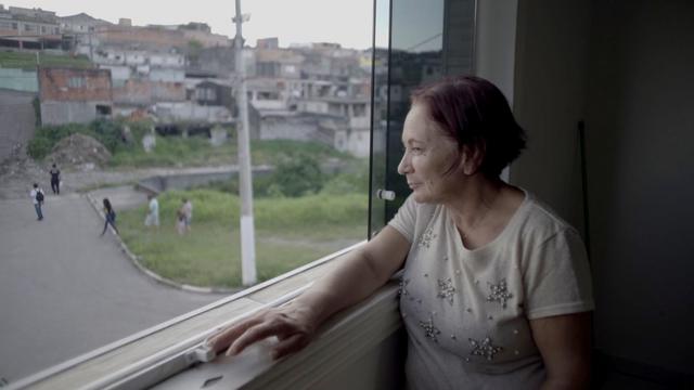 Empregada doméstica Merlene de Lima olha sua vizinhança pela janela de sua casa