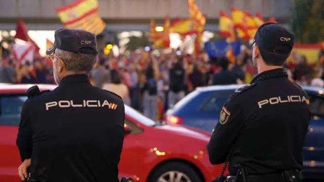 Policía mirando a gente con banderas de España, Cataluña y la Unión Europea en Barcelona.
