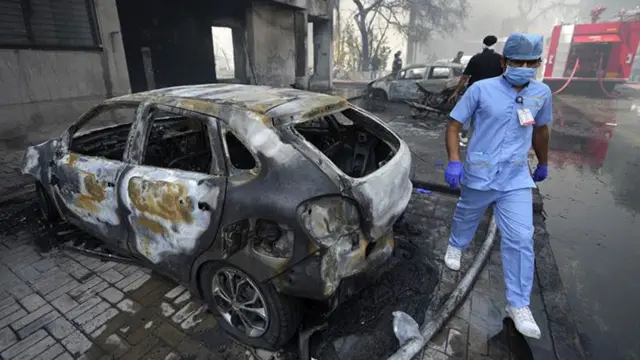 A man in medical scrubs walks beside a burnt out car A man in medical scrubs walks beside a burnt out car