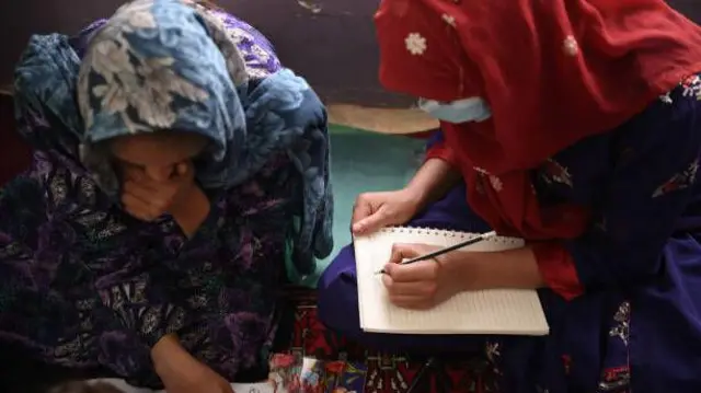 تصویر دو دختر در حال نوشتن به روی کتابچه. این دختران در حال خواندن و نوشتن اند و چهره شان در تصویر هویدا نیست.