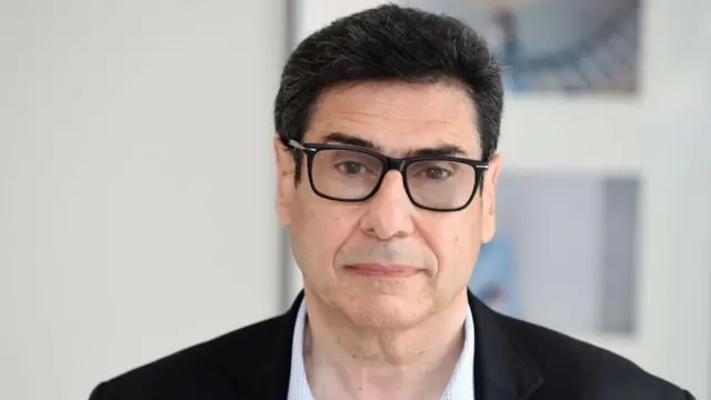 Philippe Aghion olhando para a câmera. Ele é um homem branco, de cabelos pretos, usando um óculos de grau de armação preta
