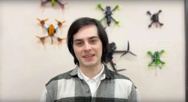 Юноша на фоне стены с прикрепленными к ней маленькими БПЛА