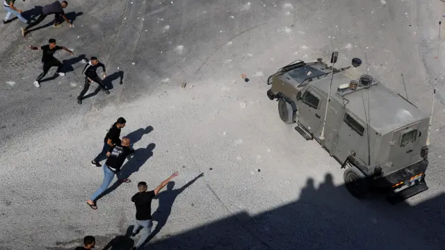 فلسطينيون يلقون بالحجارة على مركبة عسكرية إسرائيلية خلال مداهمة بالقرب من للجيش الإسرائيلي في الضفة الغربية التي تحتلها إسرائيل، 1 سبتمبر/أيلول، 2023.