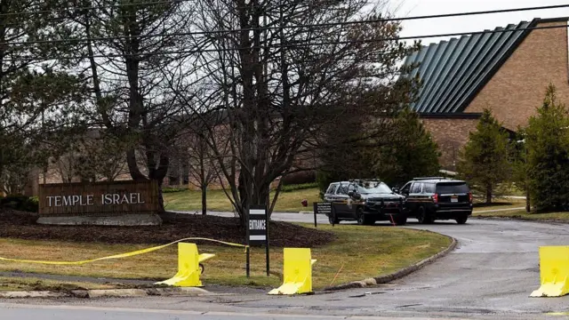 樹木の奥に建物があり、そこに続く道路に2台の車両がすれ違いの位置関係で見える。手前にはTEMPLE ISRAELの表示がある