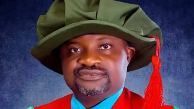 Dr Solomon Kelechi Nwafuru yi uwe emume ụbọchị nkpọkọta n'ụlọakwụkwọ na-acha uhie uhie ya na okpu na-acha akwụkwọ ndụ akwụkwọ ndụ ma nwee eriri na-acha uhie uhie. 