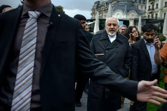 ظریف در حال راه رفتن در بین گروهی از خبرنگاران در وین در عکس دیده می‌شود. او بارانی به تن دارد و در حال حرف زدن است و ماموران امنیتی اتریشی در تلاشند تا کسی به او نزدیک نشود