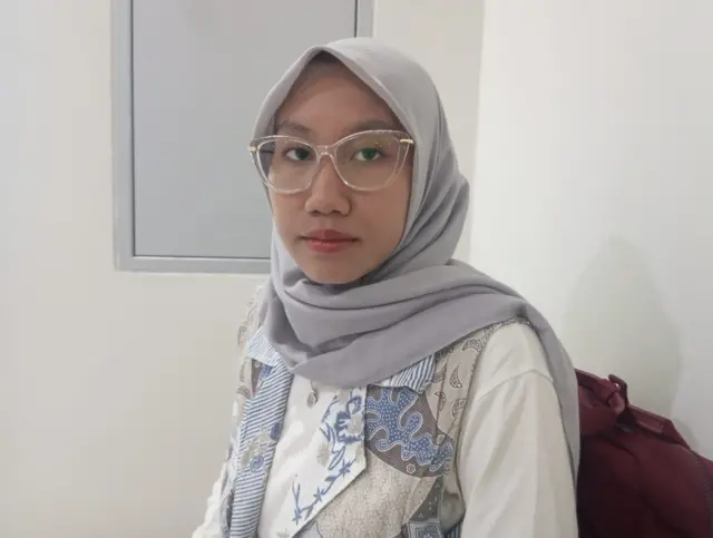 Pimpinan Umum LPM Mercusuar, Hana Fitri Lisdanta sedang mengarah ke kamera dengan hijab abu-abu dan blus bercorak batik.
