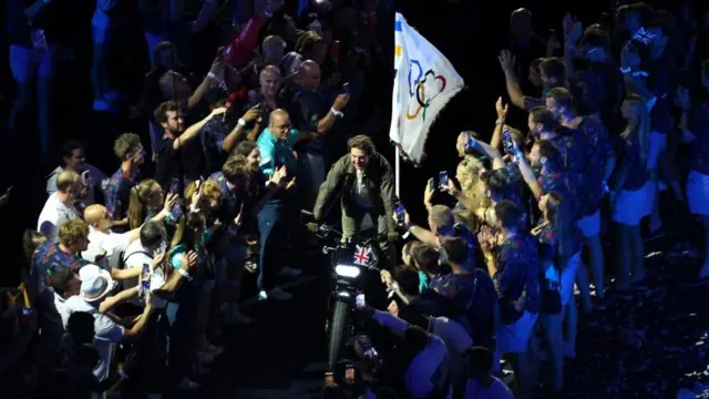 Cruise stands on the motorbike as he rides through a corridor of spectators