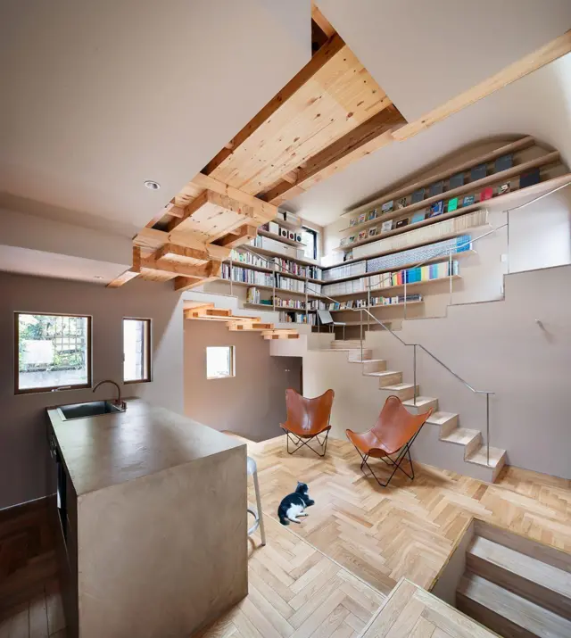 Interior de casa contemporánea con escalera integrada a una biblioteca, techos de madera vista, cocina abierta y suelo de parquet.