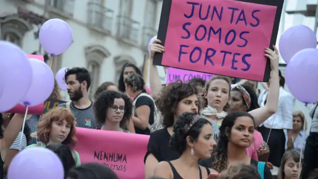 Mulheres em manifestação, uma delas com um cartaz onde se lê "Juntas somos fortes"