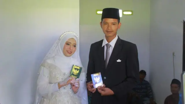 Foto pernikahan Siti Aminah dan suaminya. Pasangan ini memegang surat nikah dan memamerkannya ke kamera.