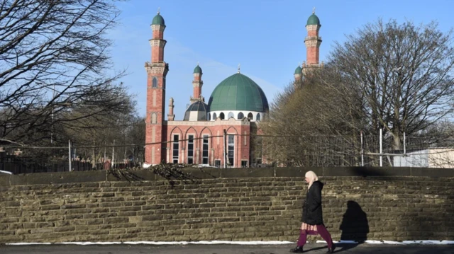 زنی در پیاده‌رو از کنار دیوار مسجدی عبور می‌کند