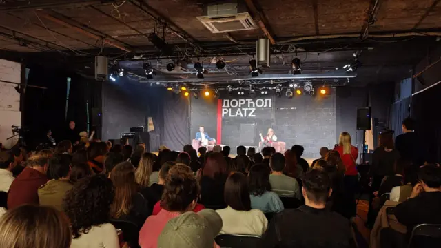 Ljudi na skupu žena na bini sedi i govori