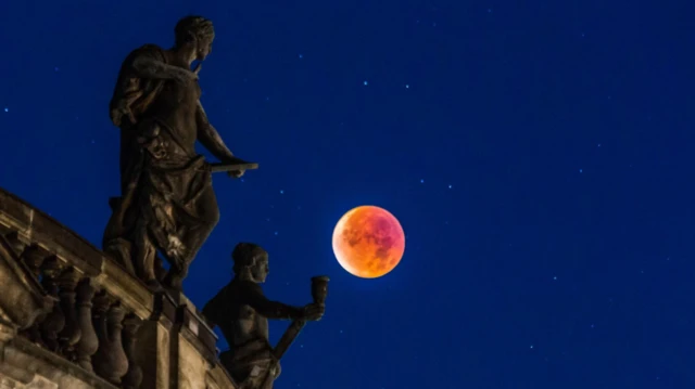 Изображение полной «кровавой Луны» 2015 года, проходящей над древним зданием на фоне тёмного синего неба