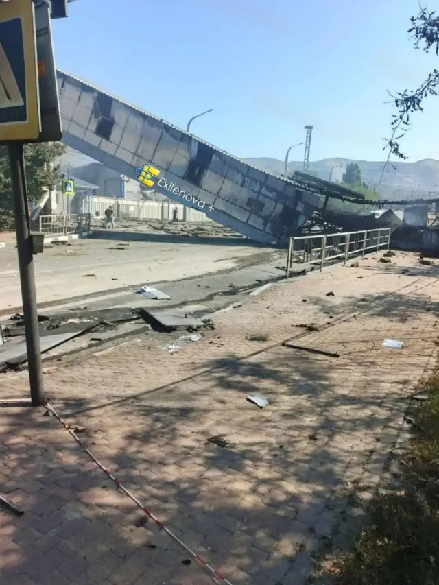 Пошкоджена внаслідок удару конструкція надземного переходу або промислової галереї, що частково обвалилася на дорогу. На місці видно уламки, пошкоджене покриття та сліди руйнувань.