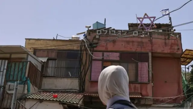 فتاة أمام منزل عليه لافتات إسرائيلية