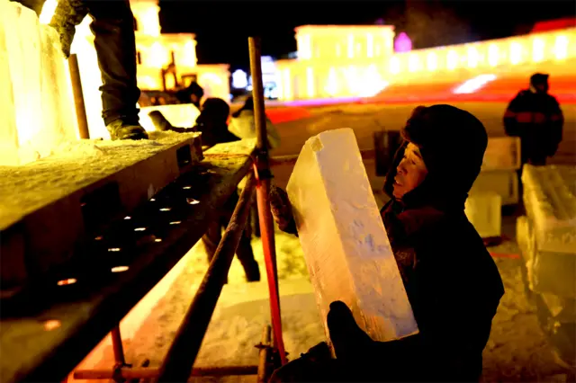 A worker carries a block of ice while building an ice structure