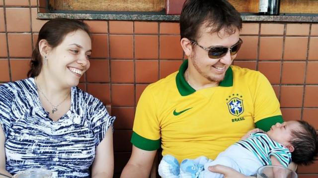 Mariana Franco e Juliano Lustosa sorriem olhando para o bebê Davi