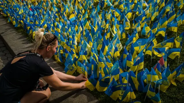 A woman sticks a flag in the Maidan Square lawn with a name of a person who died during the Russian invasion on it. Kyiv, Ukraine, August 23, 2022