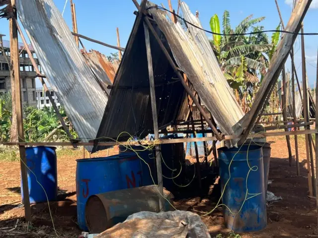 Un piège en attente de la tombée de la nuit. Il est fromé de tôles inclinées en V pour canaliser les sauterelles qui tombent dans ces fûts propres placés à leur base.