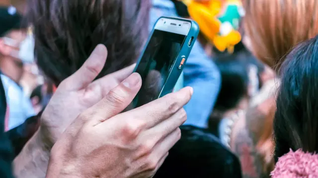 Ludzkie dłonie trzymające smartfon w tłumie