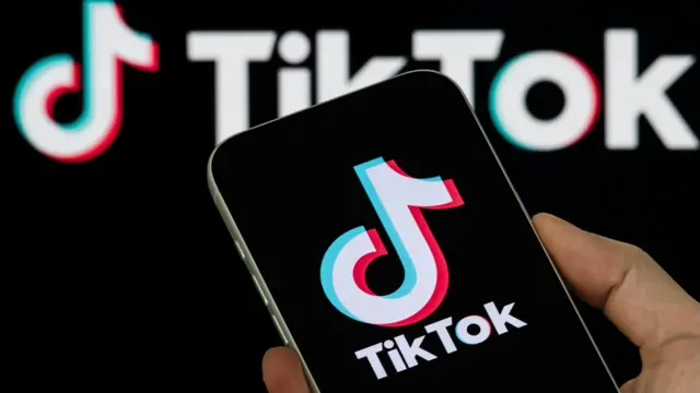 A TikTok-logó egy okostelefon képernyőjén, fekete háttér előtt, amelyen az alkalmazás logójának nagyobb változata látható.