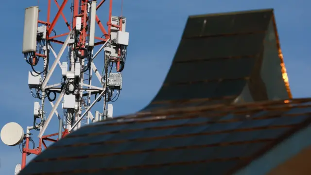 На переднем фоне - скат крыши. На заднем - башня с антеннами сотовой связи на фоне голубого неба.