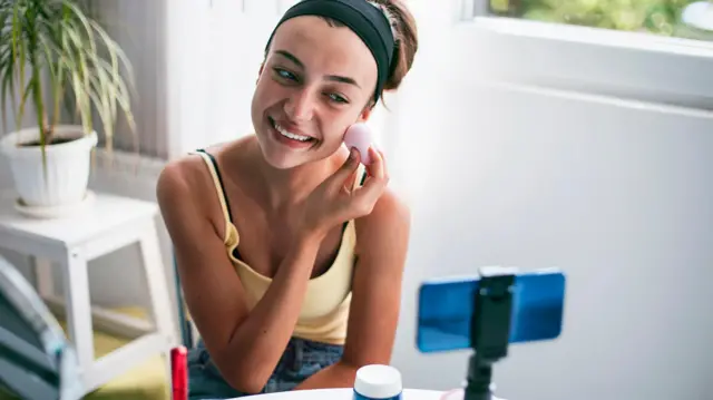 Una joven maquillándose frente a un celular. 