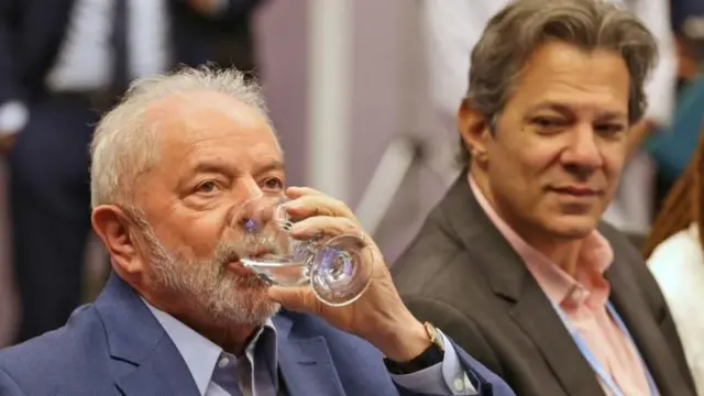 Haddad sorri contindamente ao olhar Lula beber copo d'água