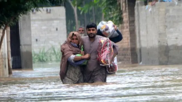 Displaced people wade through a flooded area in Peshawar, Khyber Pakhtunkhwa province