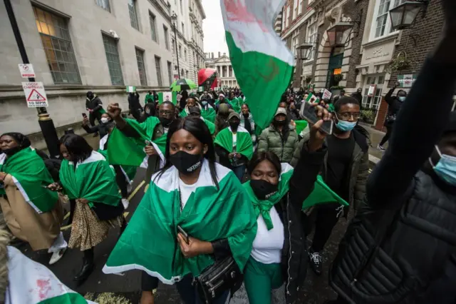 A group of Nigerians protesting on the streets wrapping the Nigerian flag around themselves.