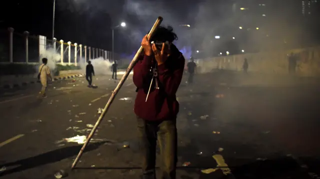 Salah seorang pendemo menuntup mukanya saat polisi melepaskan gas air mata dalam unjuk rasa pada Sabtu (30/08).